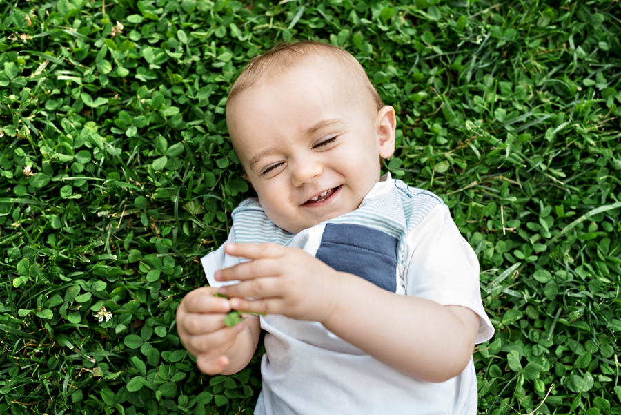 A baby boy laughing while laying in the grass.